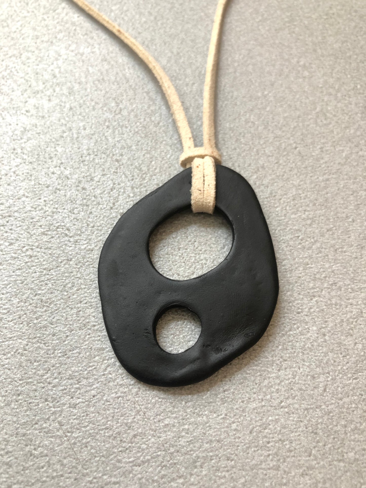Forma fluida e organica del ciondolo Due Respiri in porcellana nera con cordino beige – design handmade sensoriale