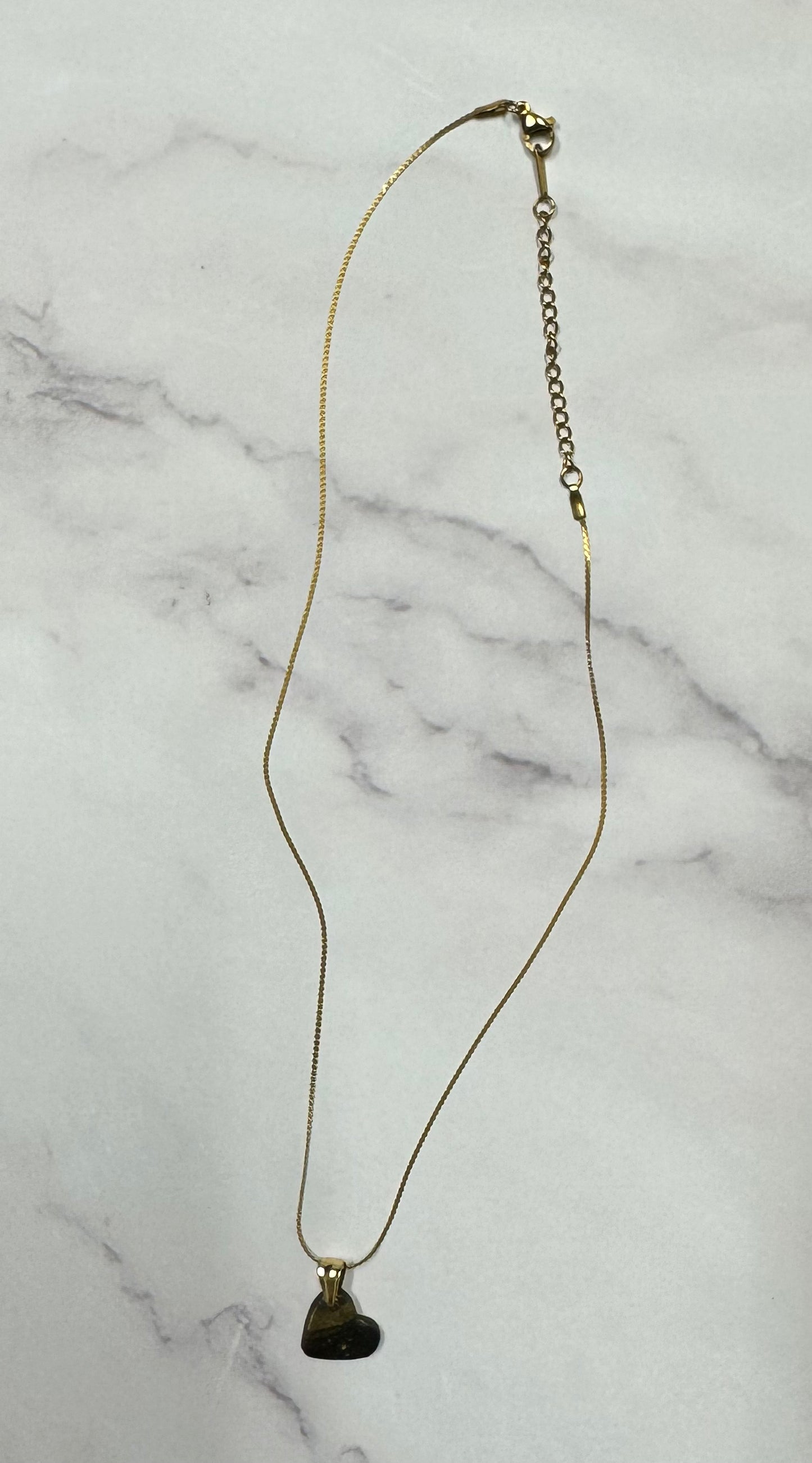 Collana cuoricino nero con brillantini oro, catena intera adagiata su sfondo marmo.