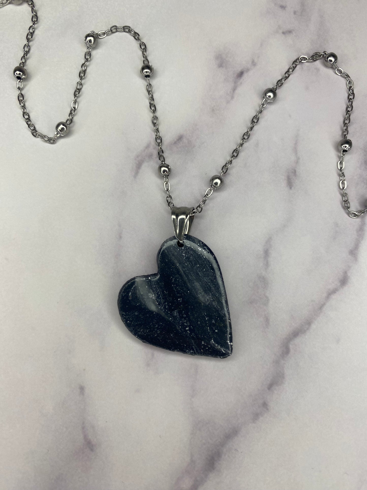 Collana pendente con ciondolo a forma di cuore, in porcellana fredda, colore nero con dettagli in argento, effetto marmo, con catenina argentata.
Gioiello artigianale fatto a mano da persone cieche e ipovedenti.