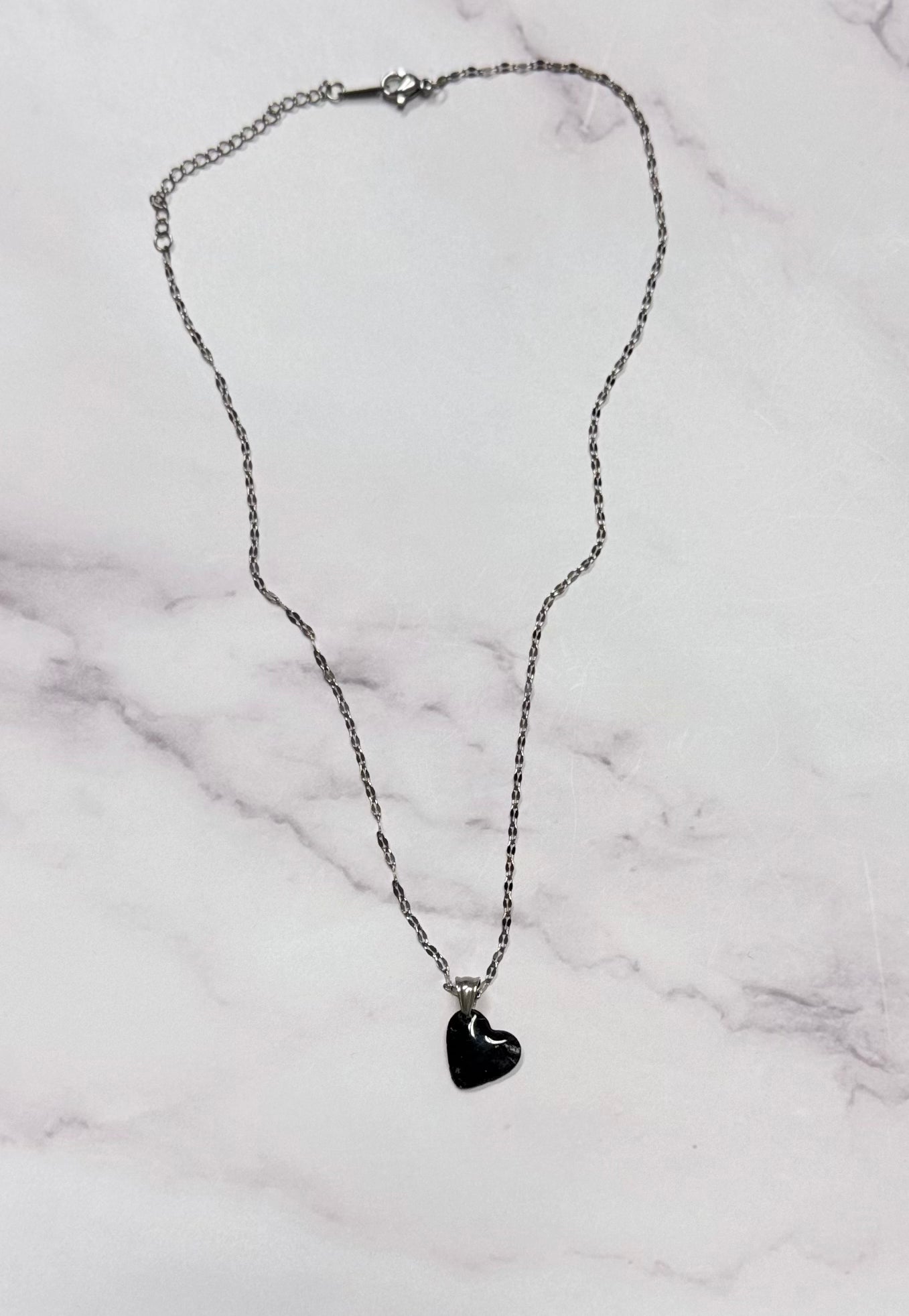 Collana dorata con ciondolo a cuore, nero con leggere sfumature argentate in porcellana fredda, adagiata su fondo marmoreo. Creata da artigiani ciechi e ipovedenti
