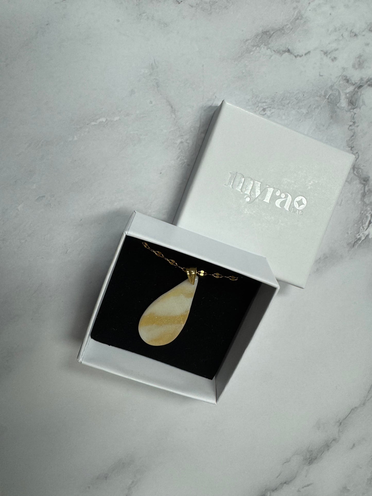 Confezione regalo aperta Myra Lab con collana pendente a goccia bianca e oro. Gioiello artigianale fatto a mano da persone cieche e ipovedenti.