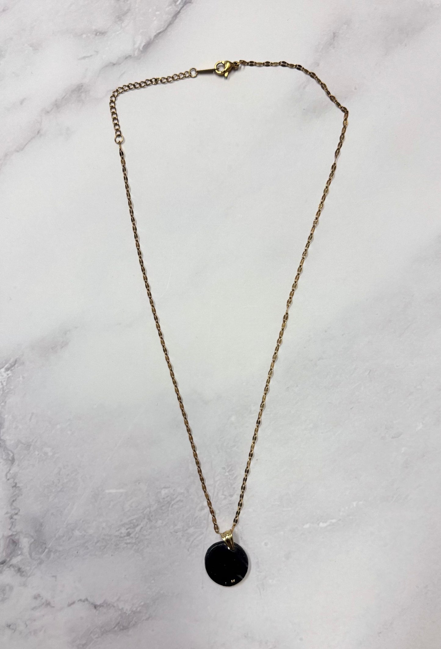 Collana con catenina dorata e pendente tondo nero in porcellana fredda e glitter, adagiata su fondo marmoreo. Creata da artigiani ciechi e ipovedenti.