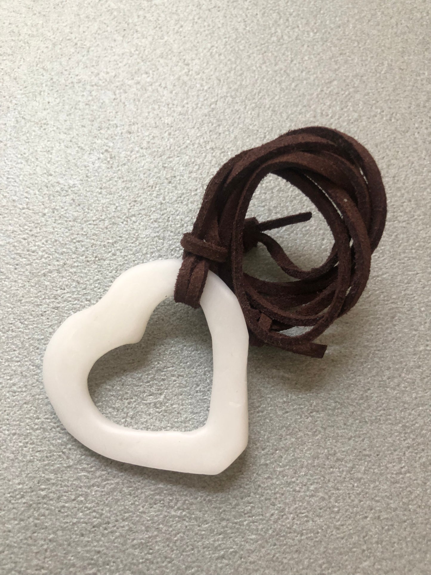 Collana “Cuore Piatto” della collezione Asimmetrie, ciondolo bianco a forma di cuore piatto in porcellana fredda con cordino marrone scuro arrotolato.