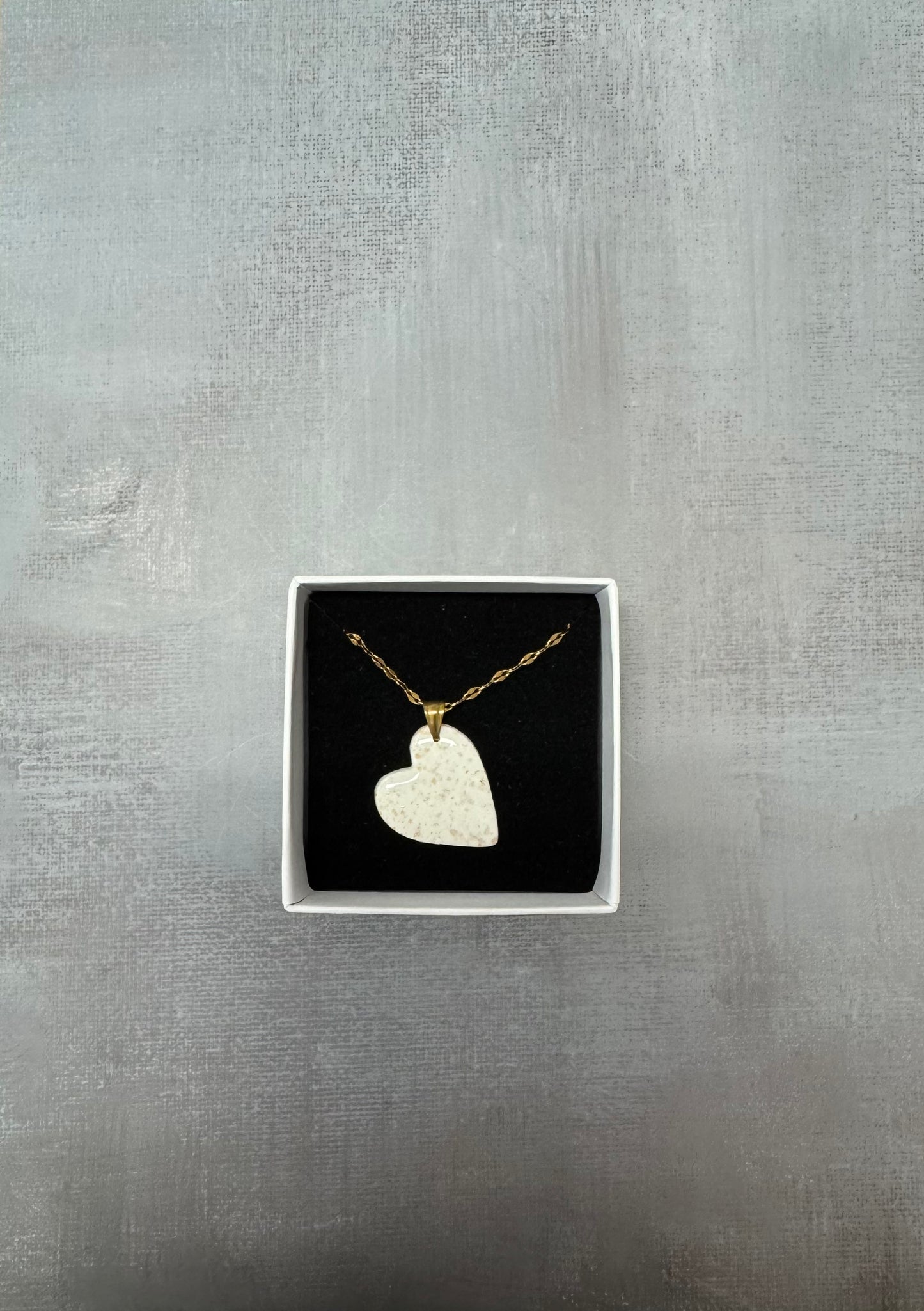 Confezione regalo aperta Myra Lab con collana pendente a cuore in porcellana fredda bianca a pois dorati. Gioiello artigianale fatto a mano da persone cieche e ipovedenti.