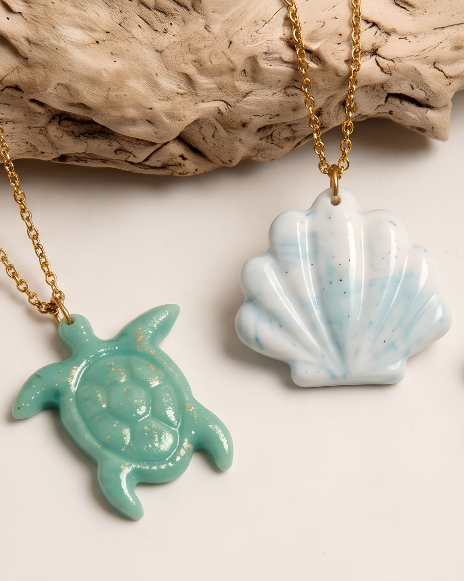 Due collane artigianali con ciondoli in porcellana fredda della collezione mare: un ciondolo a forma di conchiglia bianca con sfumature azzurre e un ciondolo a forma di tartaruga marina color verde acqua.
