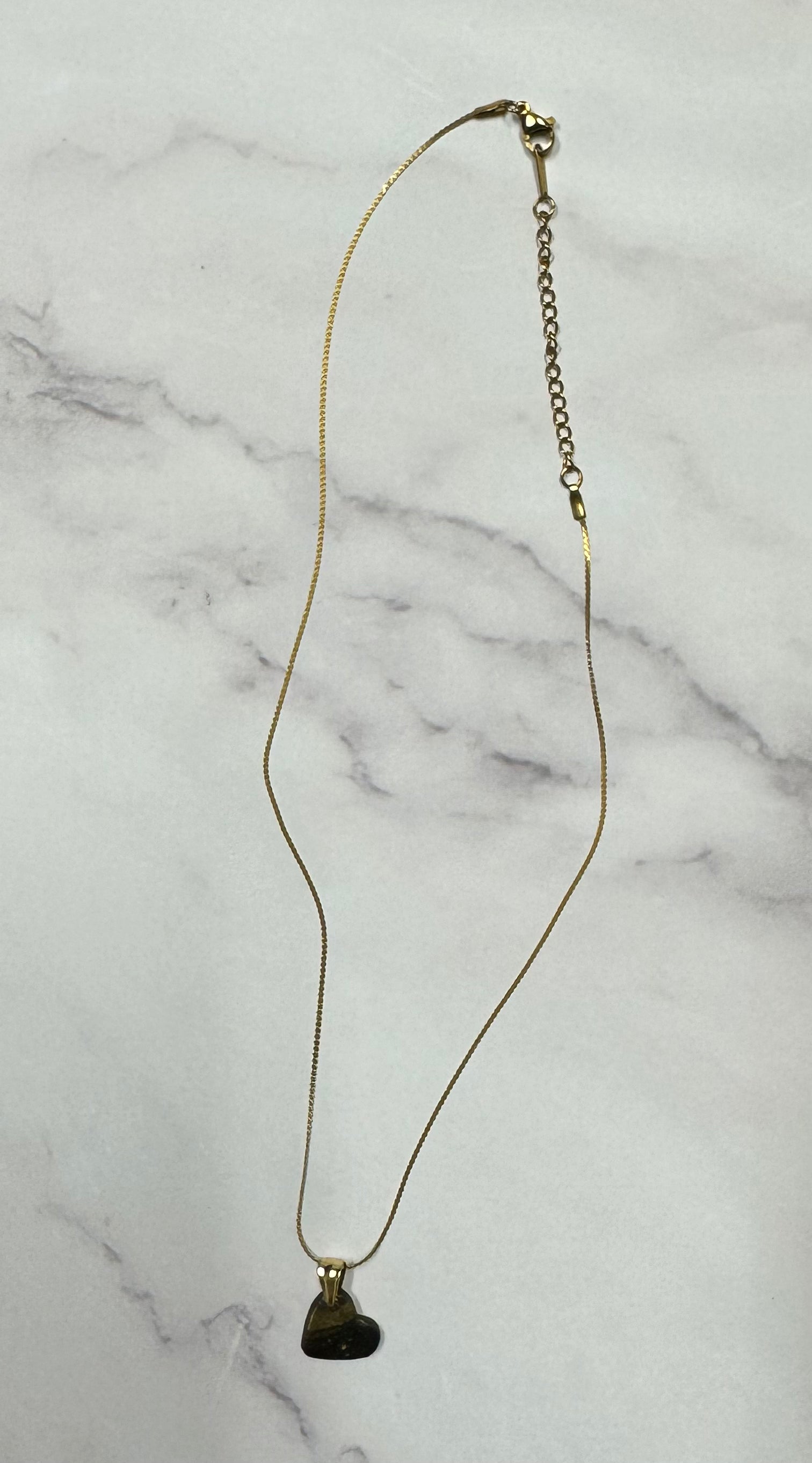 Collana cuoricino nero con brillantini oro, catena intera adagiata su sfondo marmo.