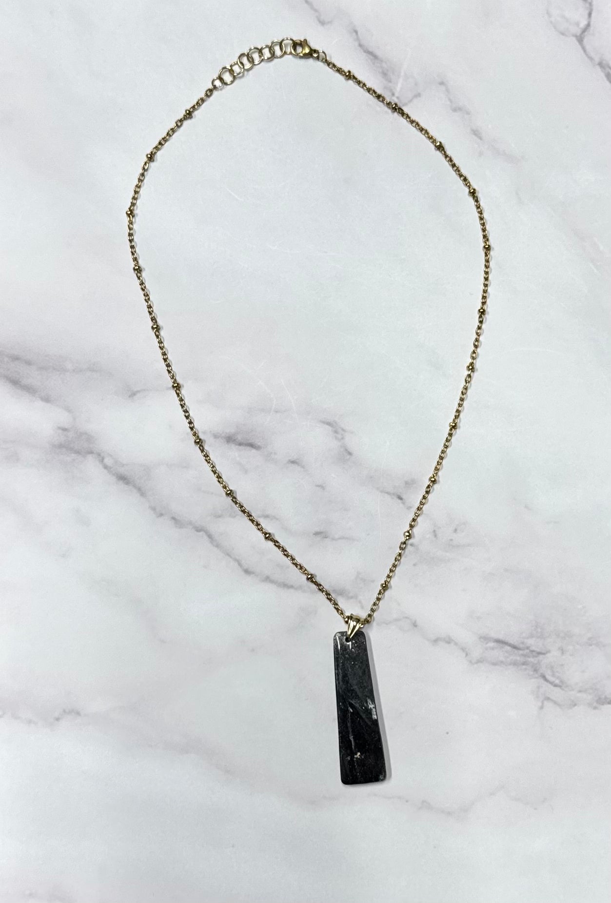 Collana rettangolo nera e oro, catena intera adagiata su sfondo marmo.