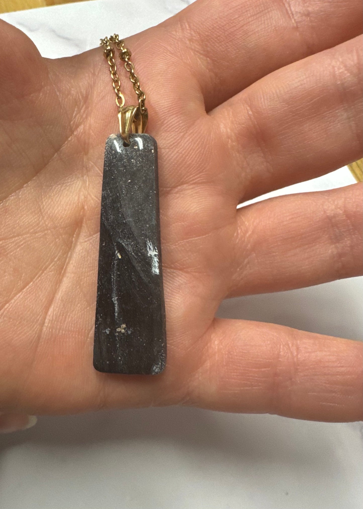 Ciondolo rettangolare nero effetto marmo appoggiato sul palmo di una mano, catena dorata.
