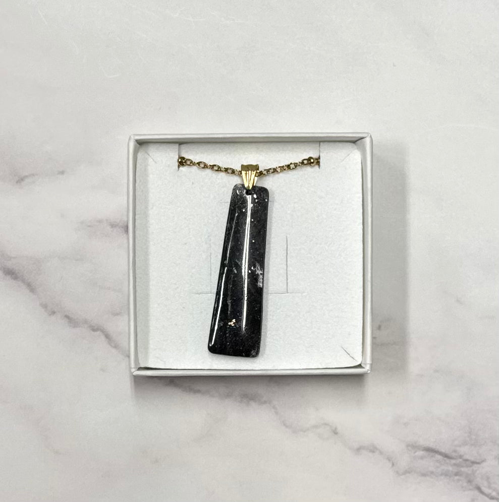Ciondolo rettangolare nero effetto marmo, catena dorata, in scatolina regalo bianca aperta su sfondo marmo.