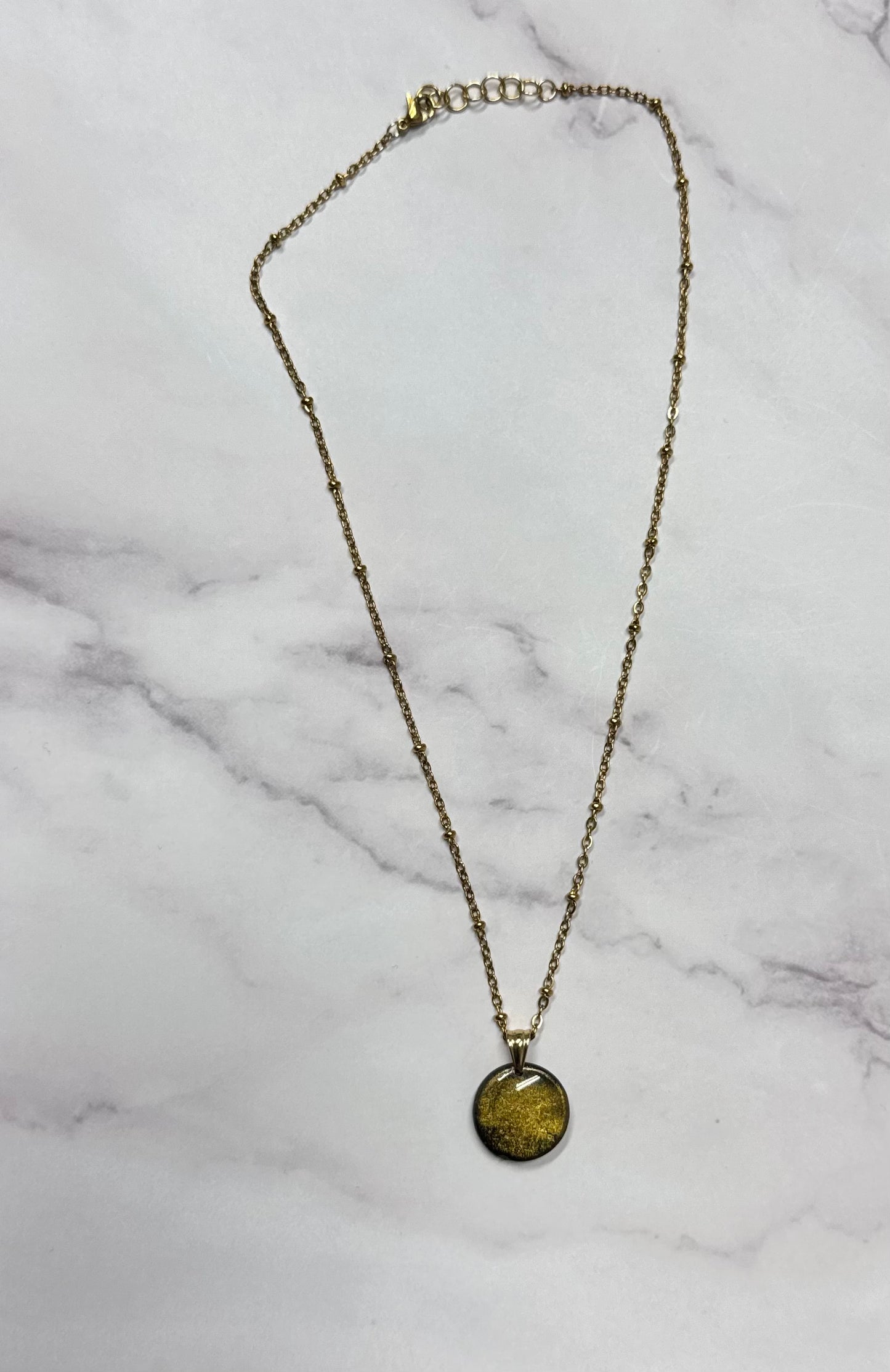 Collana a cerchio dorato, catena intera adagiata su sfondo marmo.