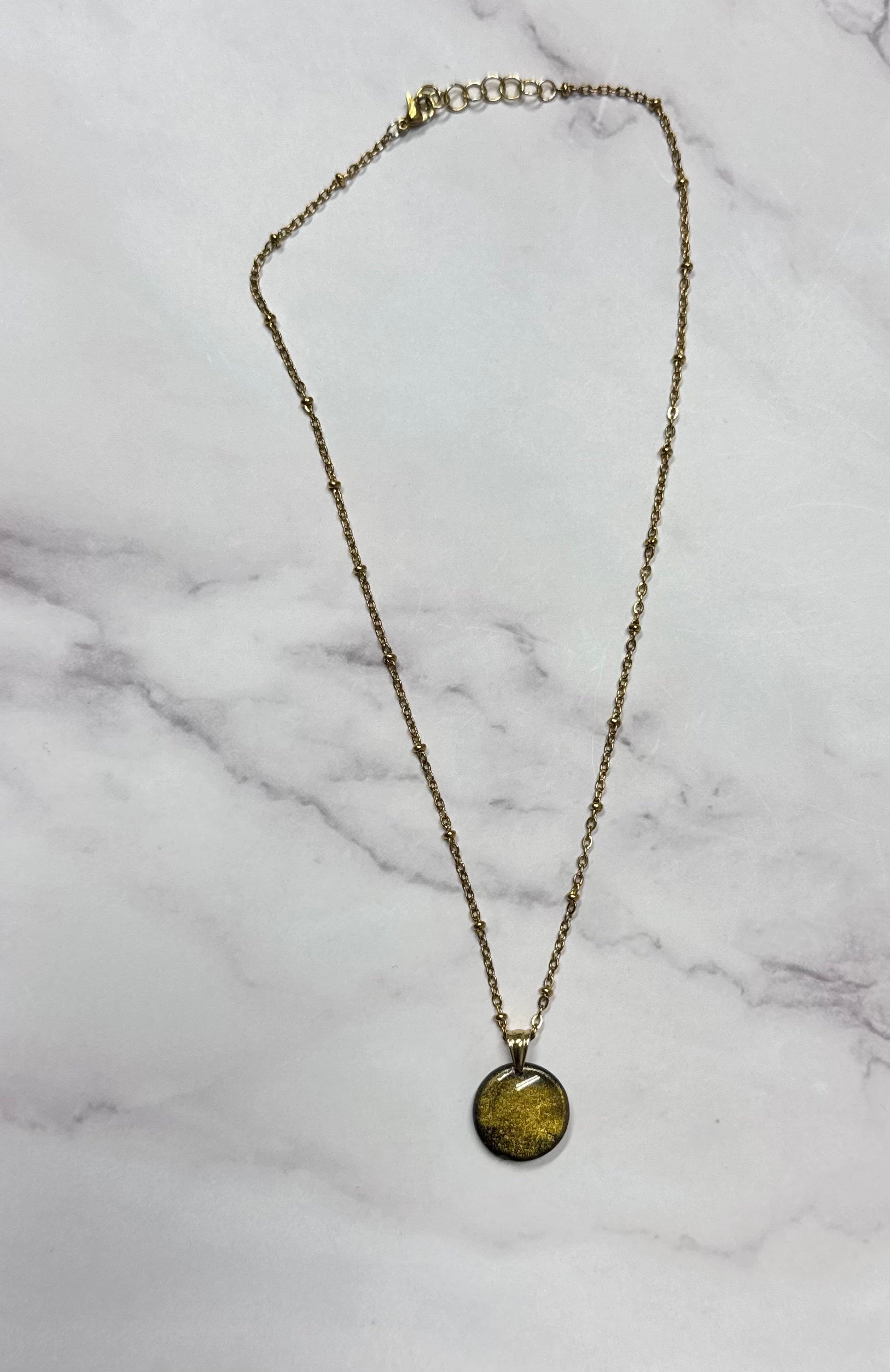 Collana a cerchio dorato, catena intera adagiata su sfondo marmo.