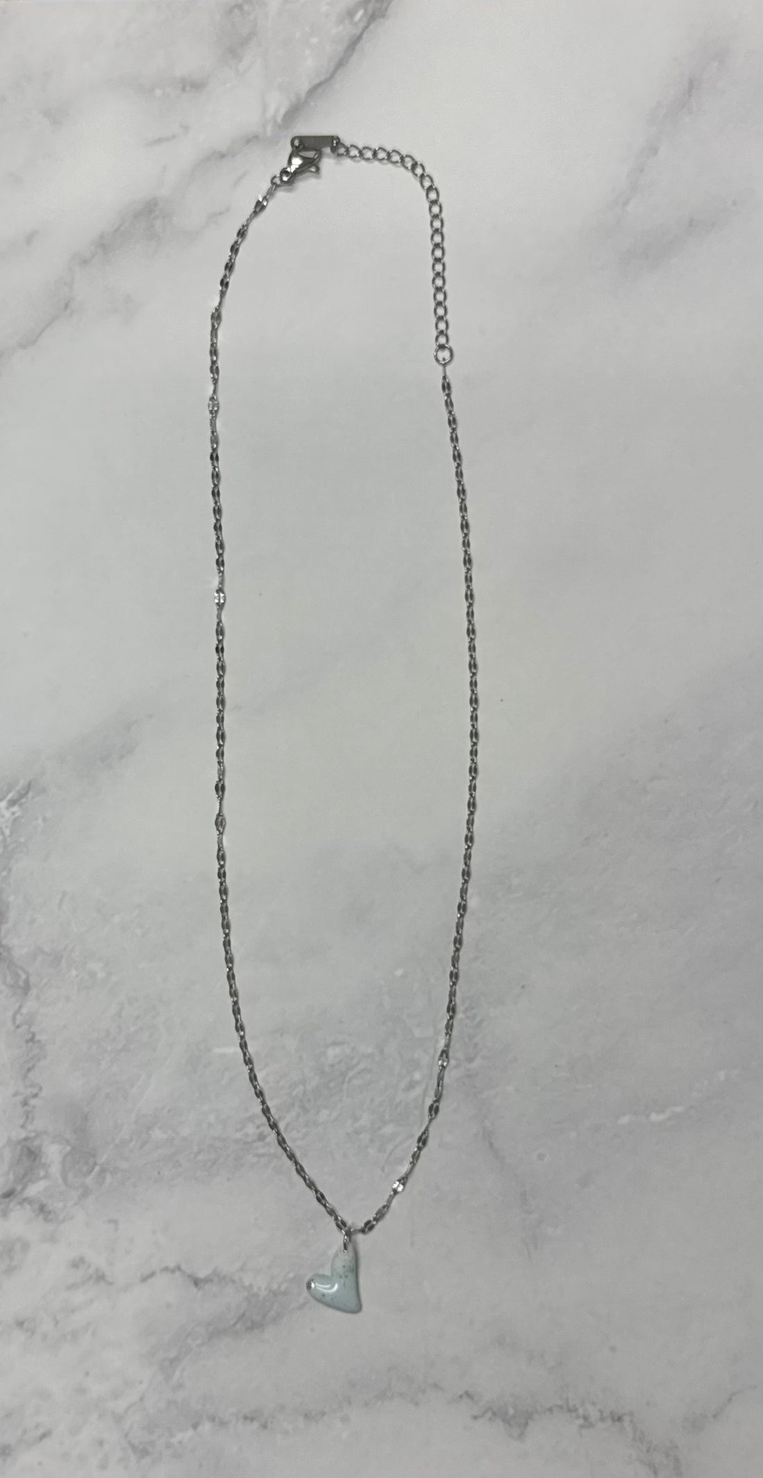 Collana Cuore azzurra, catena argentata intera adagiata su sfondo marmo.