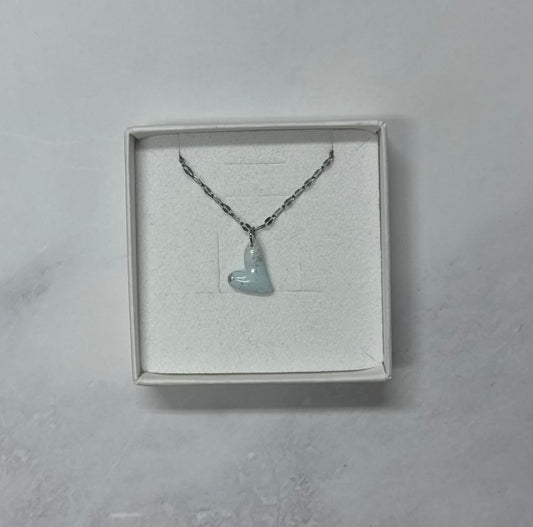 Ciondolo a cuore azzurro tenue con texture screziata, catena argentata, in scatolina regalo bianca aperta su sfondo marmo.