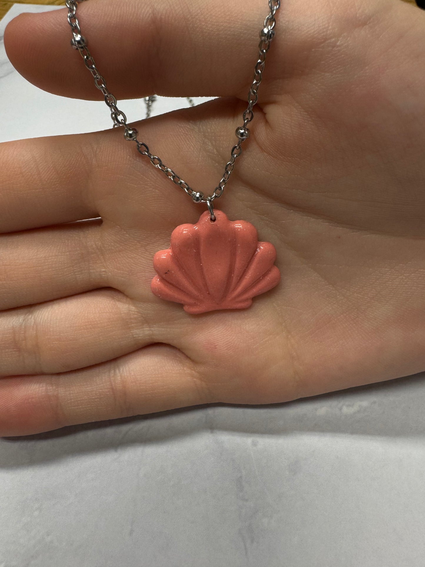 Collana Conchiglia rosa, catena argentata, dettaglio ravvicinato su sfondo marmo.