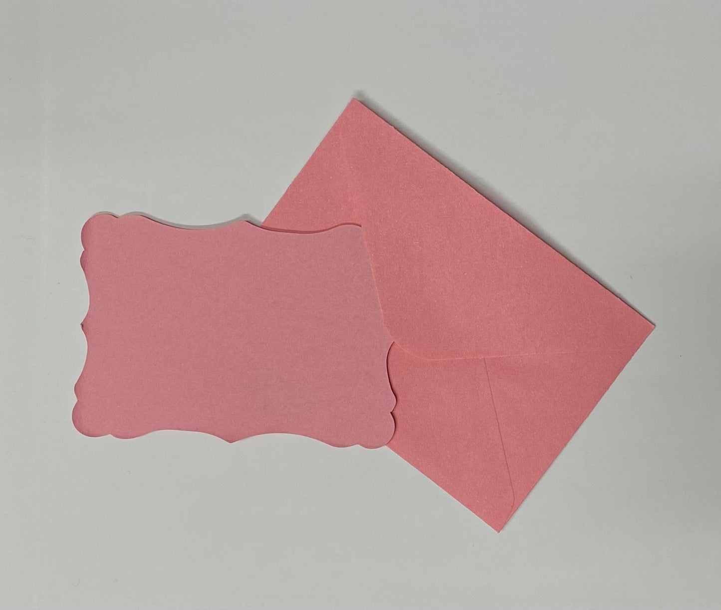 Bigliettino sagomato rosa con busta coordinata su sfondo chiaro.