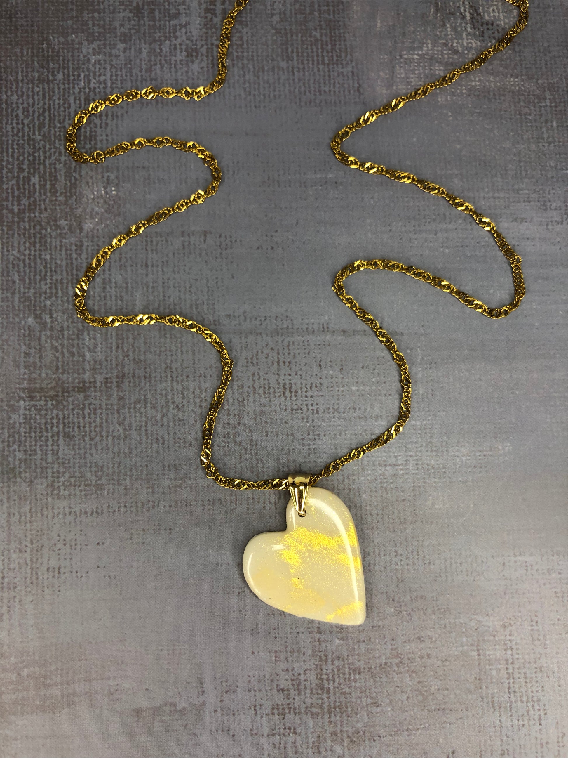 Collana pendente con ciondolo a forma di cuore, in porcellana fredda, colore bianco con dettagli in oro, con catenina dorata. 
Gioiello artigianale fatto a mano da persone cieche e ipovedenti.