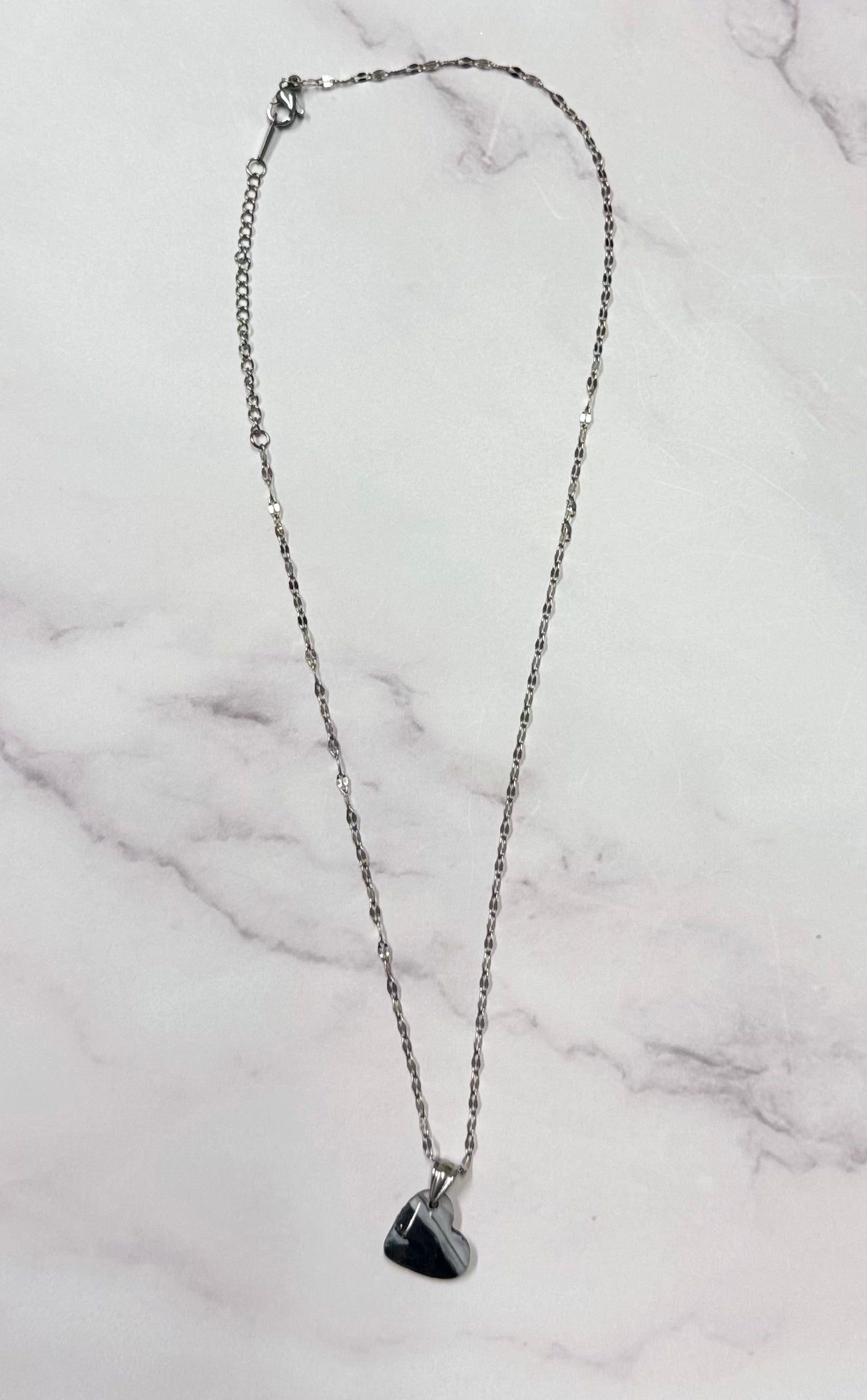 Collana con ciondolo a forma di cuore, di colore nero e bianco, in porcellana fredda, adagiata su fondo marmoreo. Creata da artigiani ciechi e ipovedenti