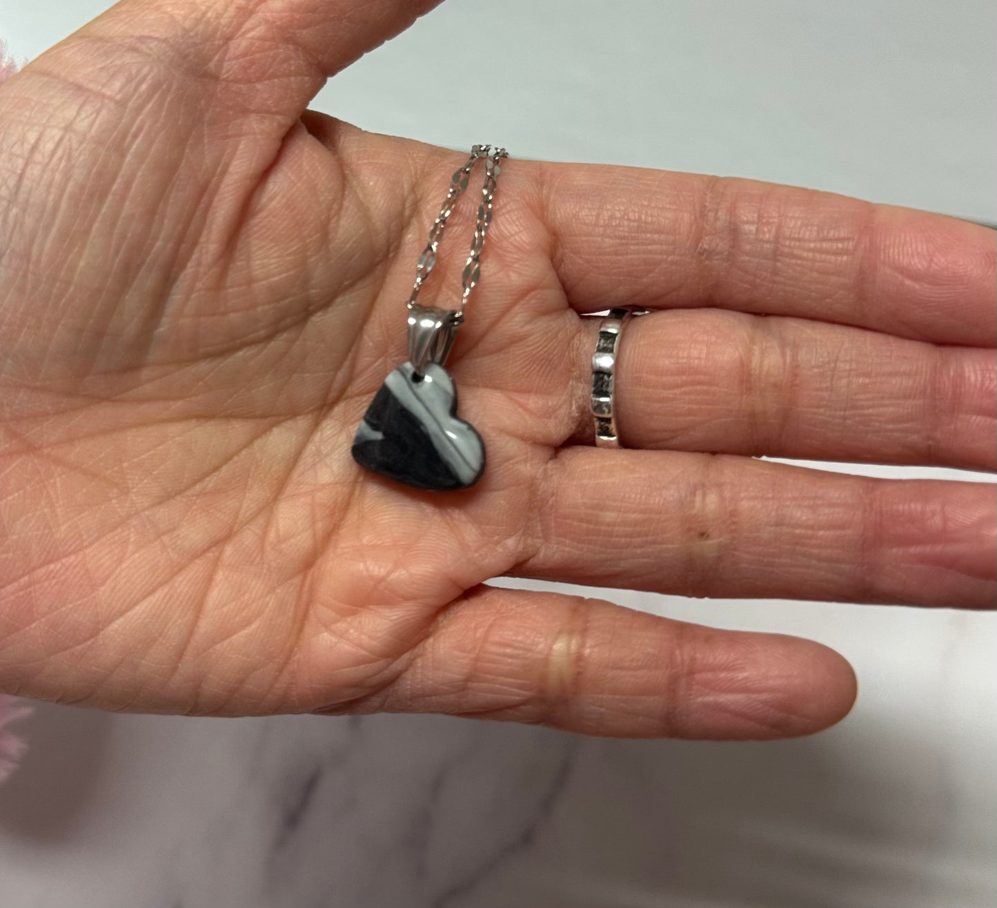 Collana con ciondolo a forma di cuore, di colore bianco e nero, in porcellana fredda, sul palmo di una mano. Gioiello realizzato da artigiani ciechi e ipovedenti.