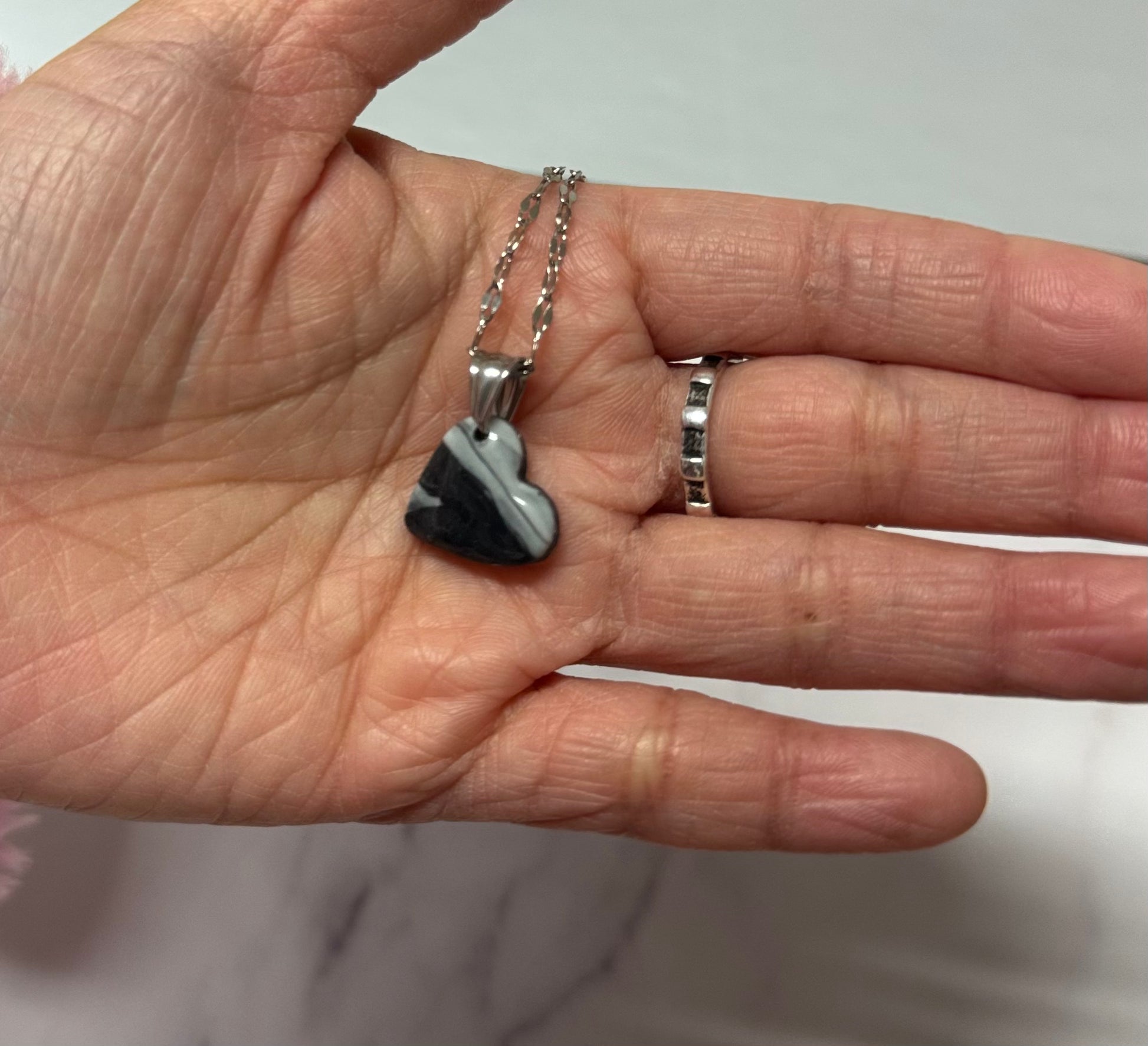 Collana con ciondolo a forma di cuore, di colore bianco e nero, in porcellana fredda, sul palmo di una mano. Gioiello realizzato da artigiani ciechi e ipovedenti.