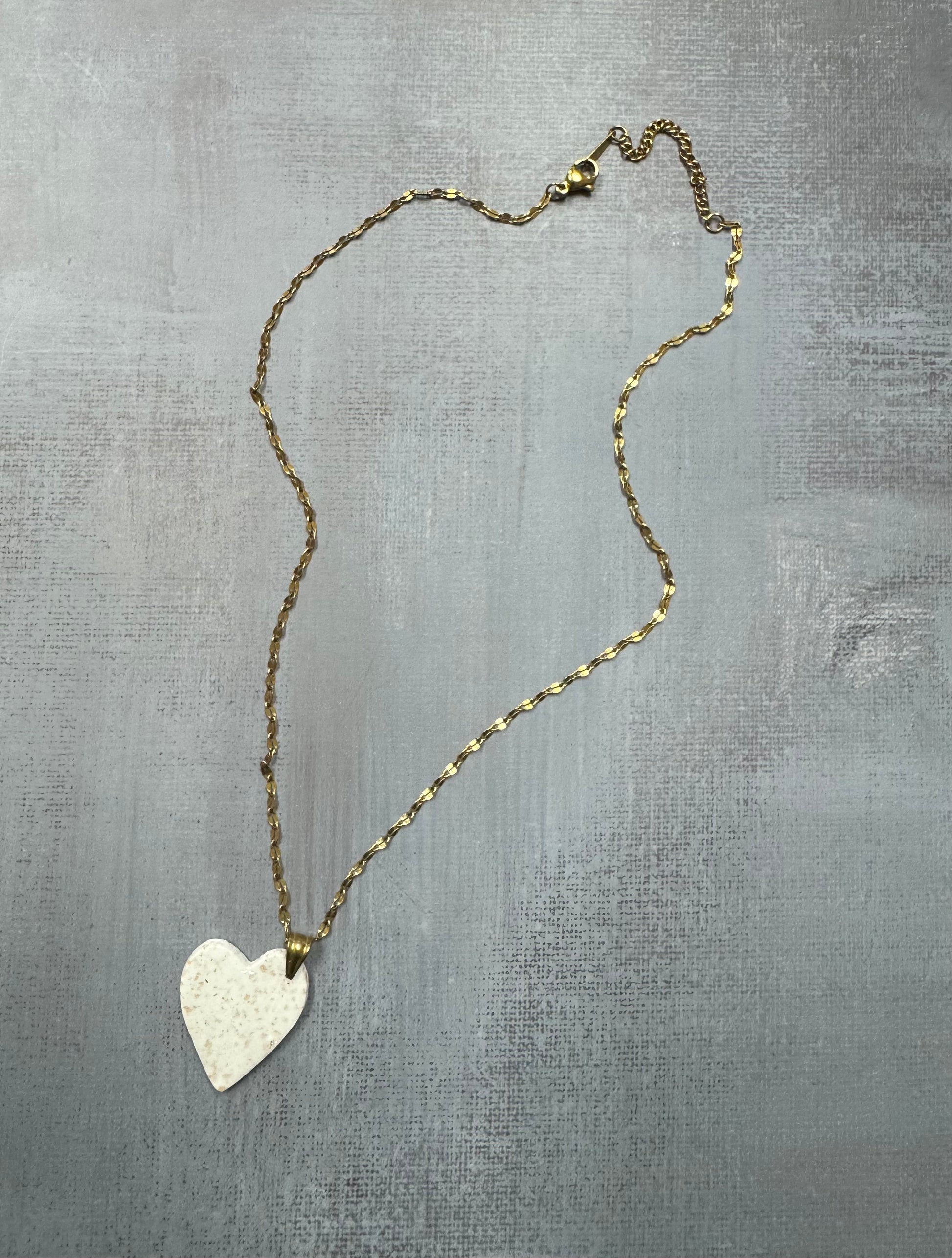 Vista d'insieme dell'intera collana pendente con ciondolo a cuore bianco a pois in porcellana fredda stesa in tutta la sua lunghezza. Gioiello artigianale fatto a mano da persone cieche e ipovedenti.
