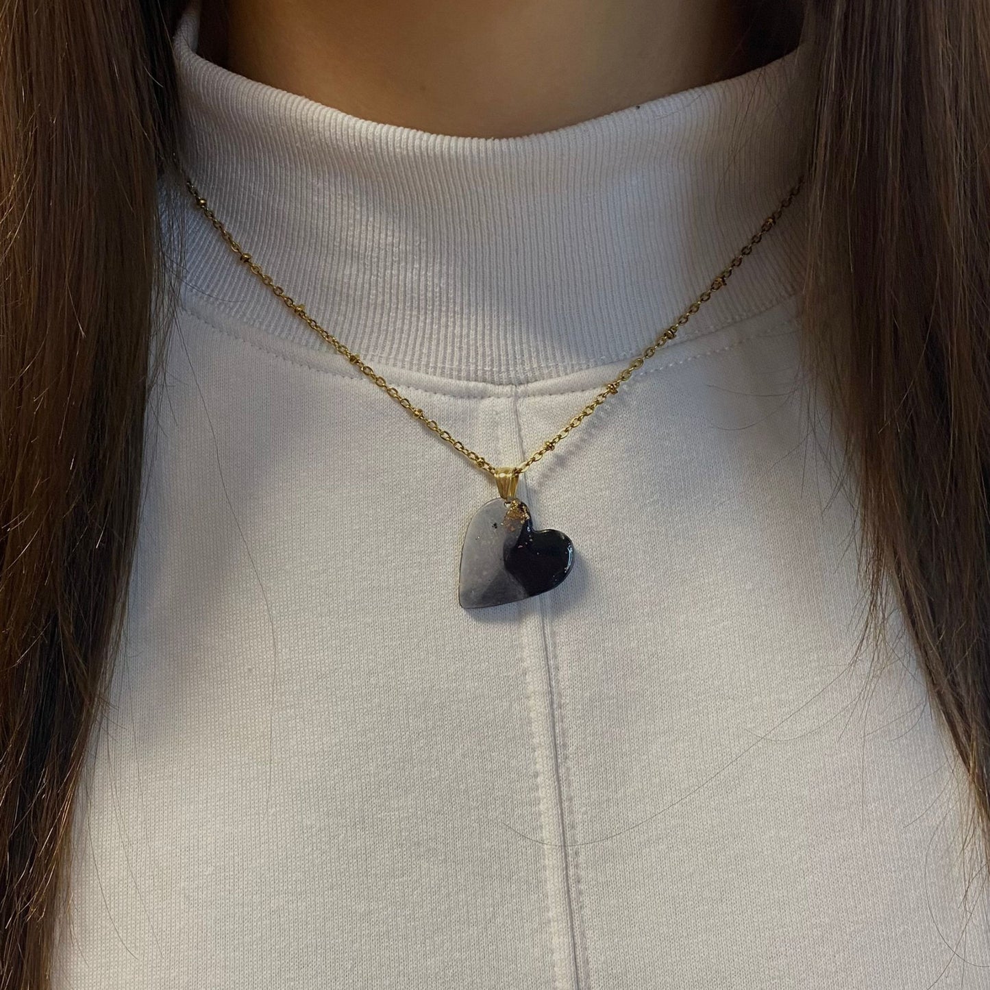 Primo piano della collana indossata su una maglietta bianca. Collana pendente con ciondolo a forma di cuore in porcellana fredda, colore nero e bianco, effetto marmo sfumato, con catenina dorata. Gioiello artigianale fatto a mano da persone cieche e ipovedenti.
