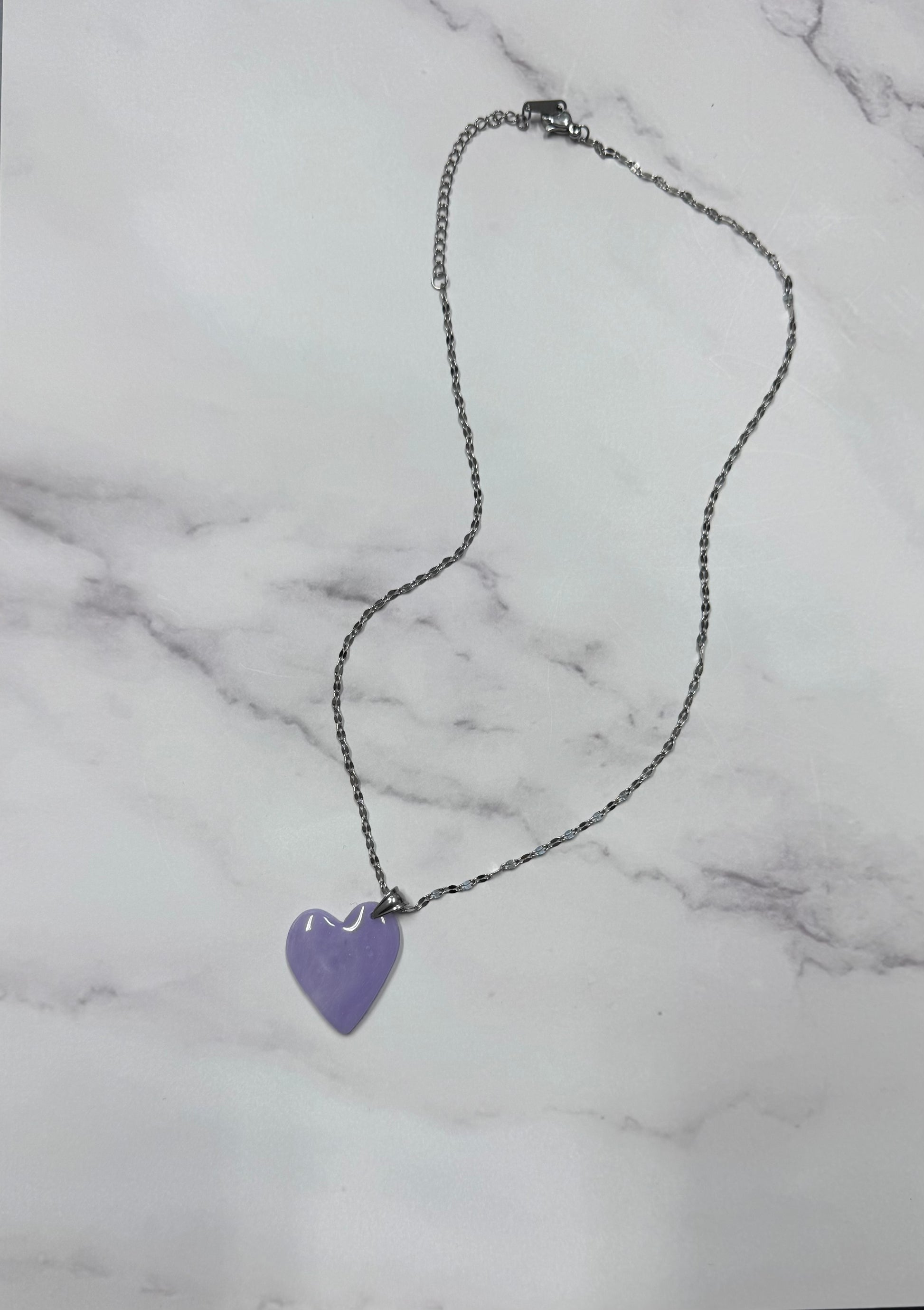 Vista d'insieme dell'intera collana pendente con ciondolo a cuore lilla in porcellana fredda,con sfumature, stesa in tutta la sua lunghezza, con catenina argentata.  Gioiello artigianale fatto a mano da persone cieche e ipovedenti.
