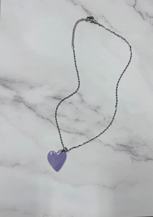 Vista d'insieme dell'intera collana pendente con ciondolo a cuore lilla in porcellana fredda,con sfumature, stesa in tutta la sua lunghezza, con catenina argentata.  Gioiello artigianale fatto a mano da persone cieche e ipovedenti.