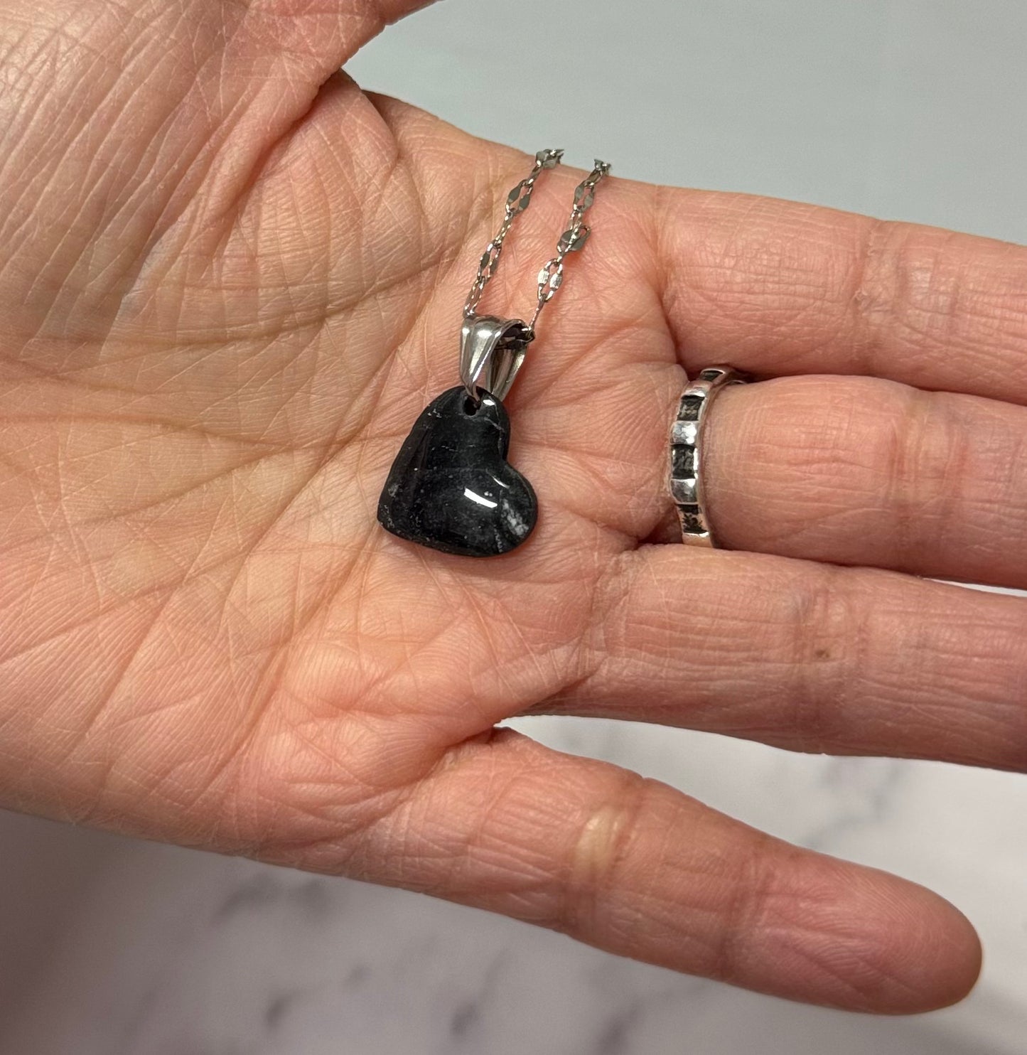 Collana con cuore nero, in porcellana fredda e leggere sfumature argentate, sul palmo di una mano. Gioiello realizzato da artigiani ciechi e ipovedenti.