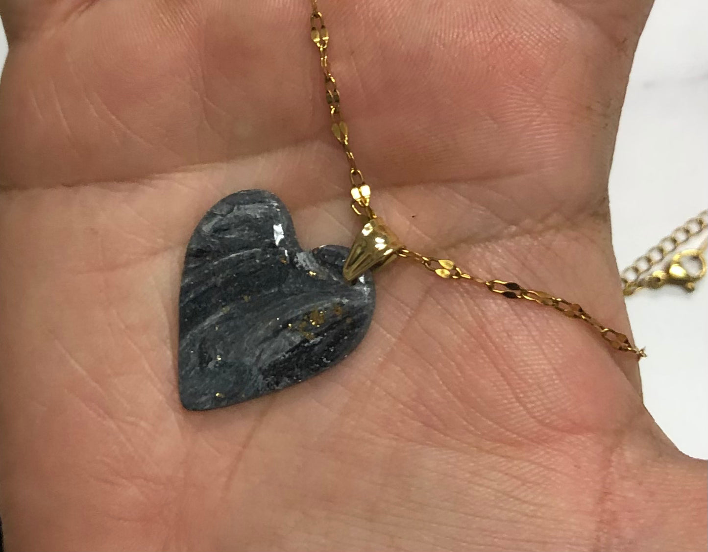 Collana con cuore nero dorato in porcellana fredda, sul palmo di una mano. Gioiello realizzato da artigiani ciechi e ipovedenti.