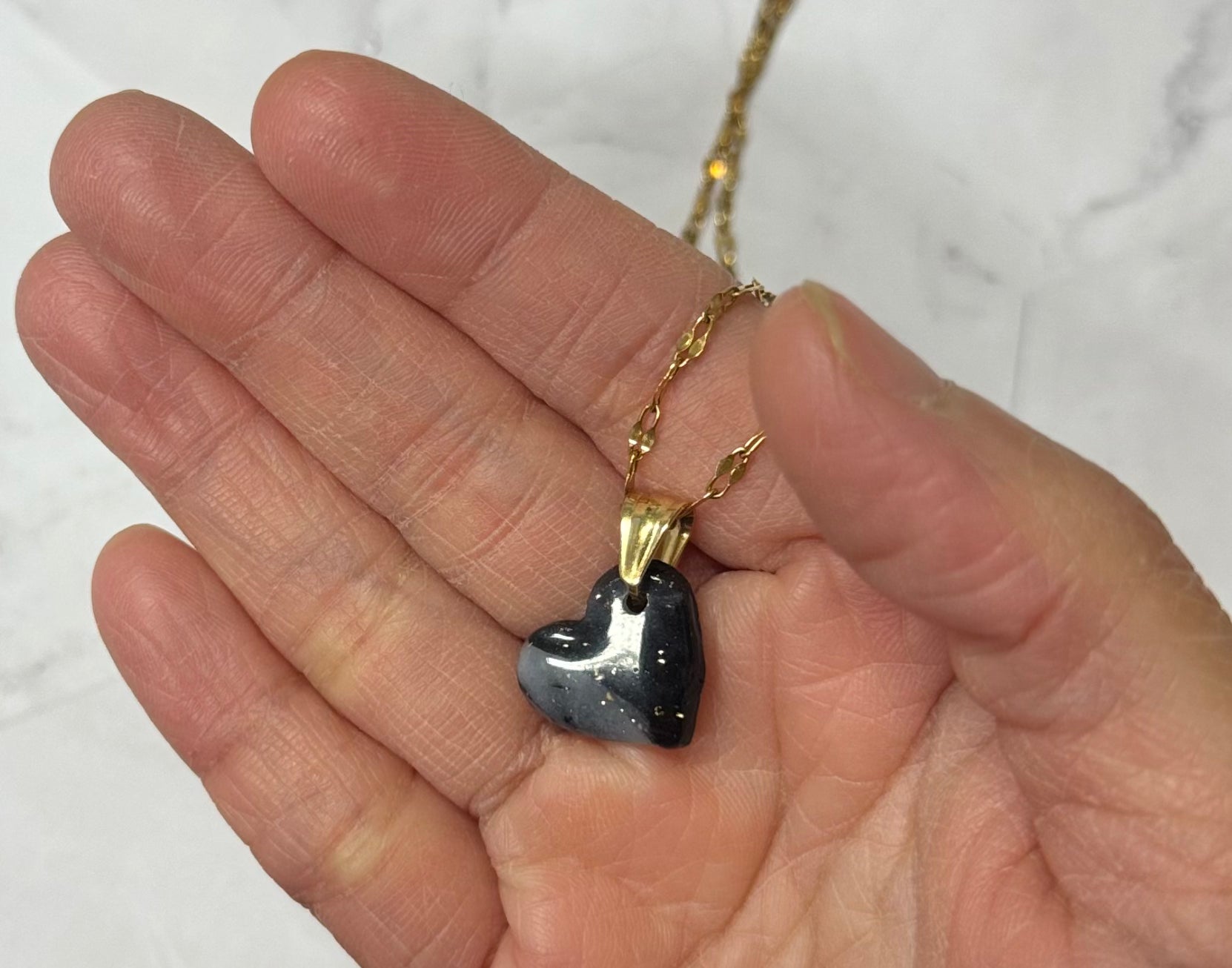 Collana con cuore nero sfumato in porcellana fredda, sul palmo di una mano. Gioiello realizzato da artigiani ciechi e ipovedenti.