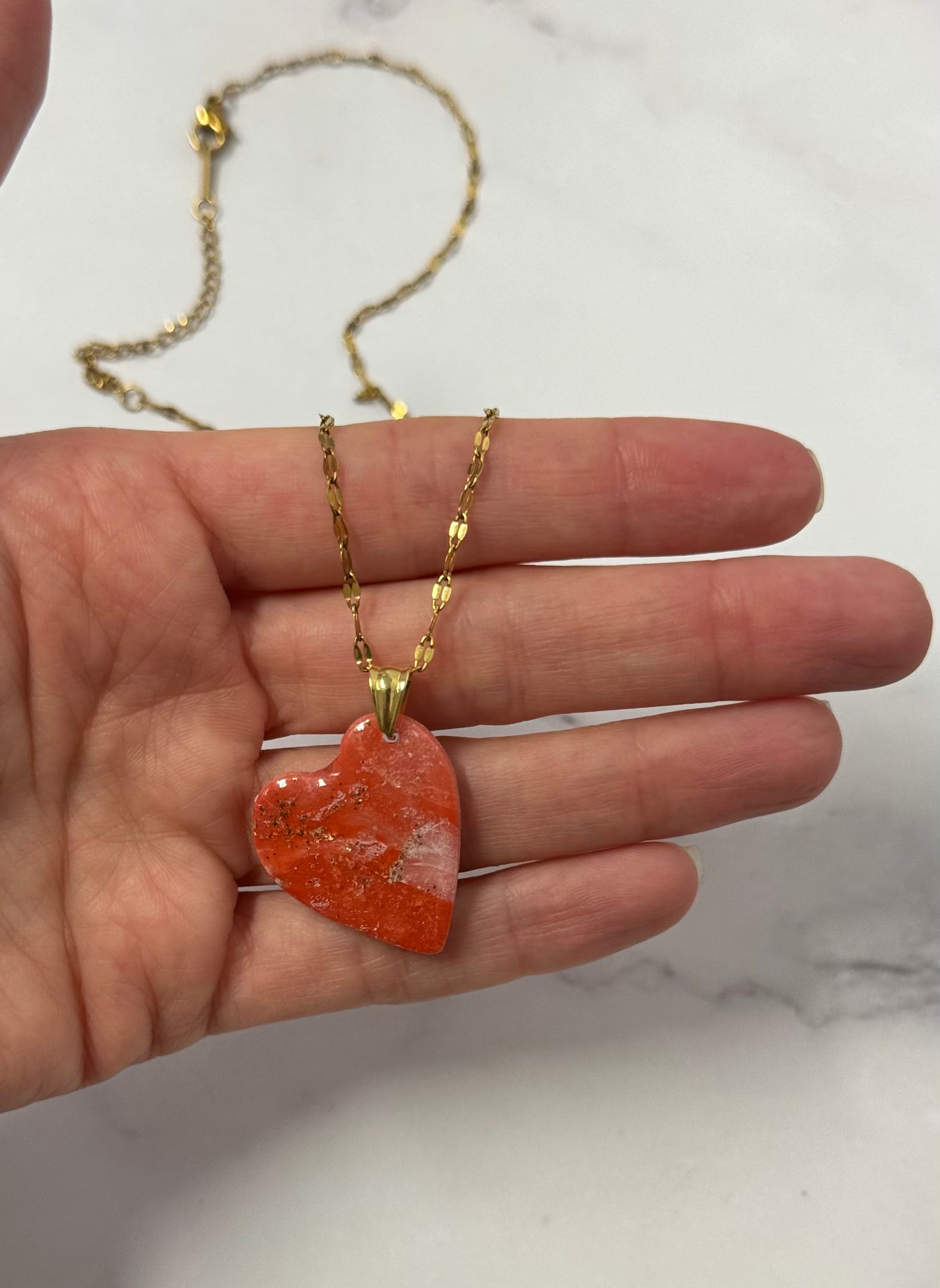 Collana con cuore rosso marmorizzato in porcellana fredda e leggere sfumature dorate, sul palmo di una mano. Gioiello realizzato da artigiani ciechi e ipovedenti.