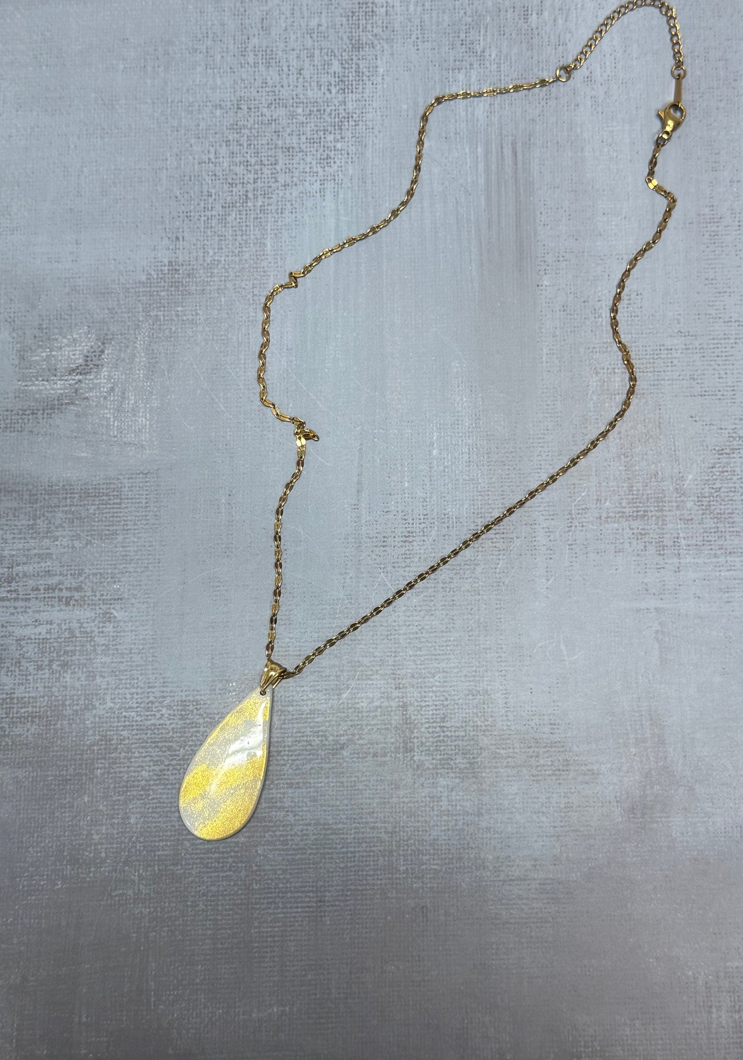 Vista d'insieme dell'intera collana pendente con ciondolo a goccia in porcellana fredda bianco e oro, stesa in tutta la sua lunghezza. Gioiello artigianale fatto a mano da persone cieche e ipovedenti.