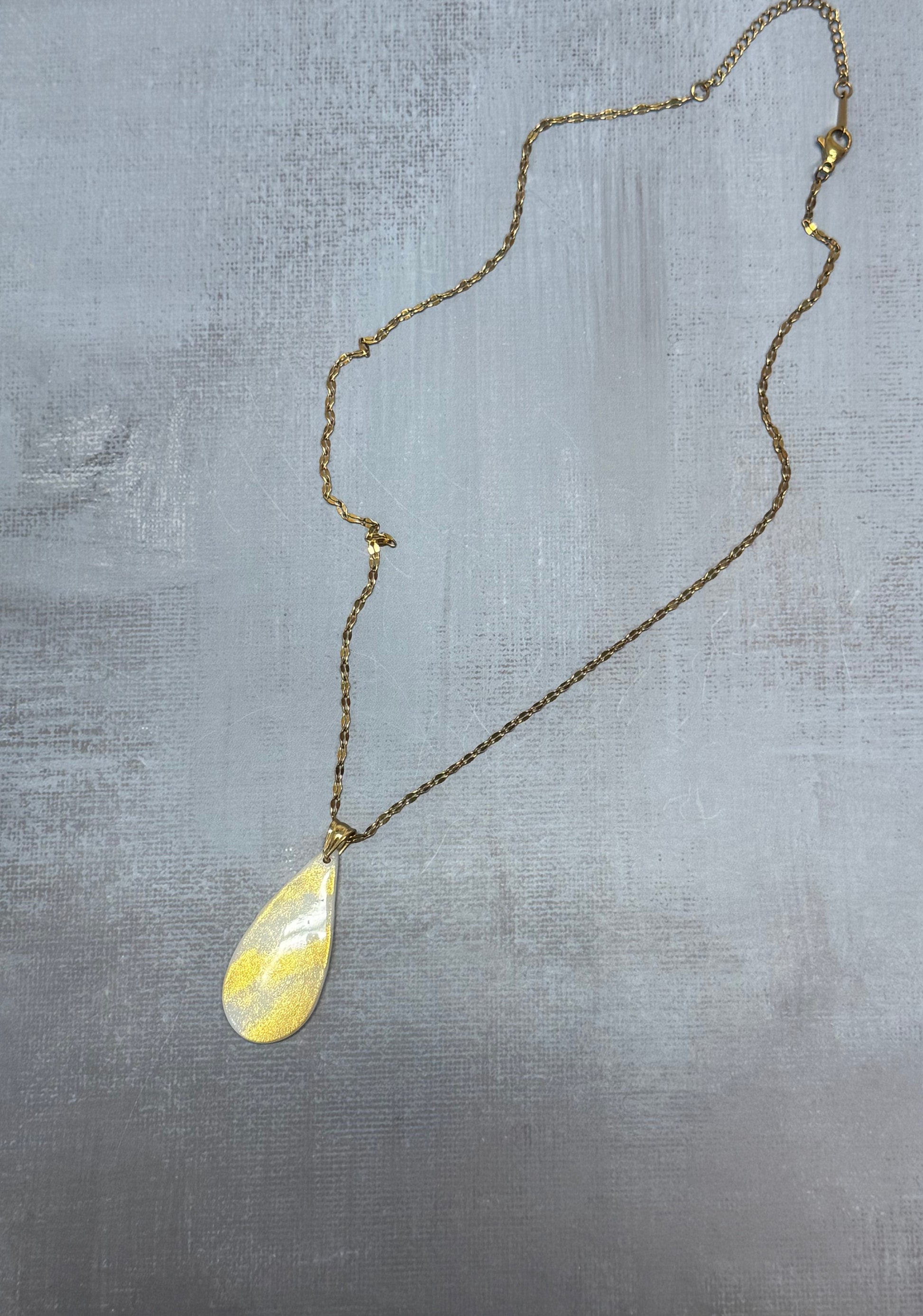 Vista d'insieme dell'intera collana pendente con ciondolo a goccia in porcellana fredda bianco e oro, stesa in tutta la sua lunghezza. Gioiello artigianale fatto a mano da persone cieche e ipovedenti.