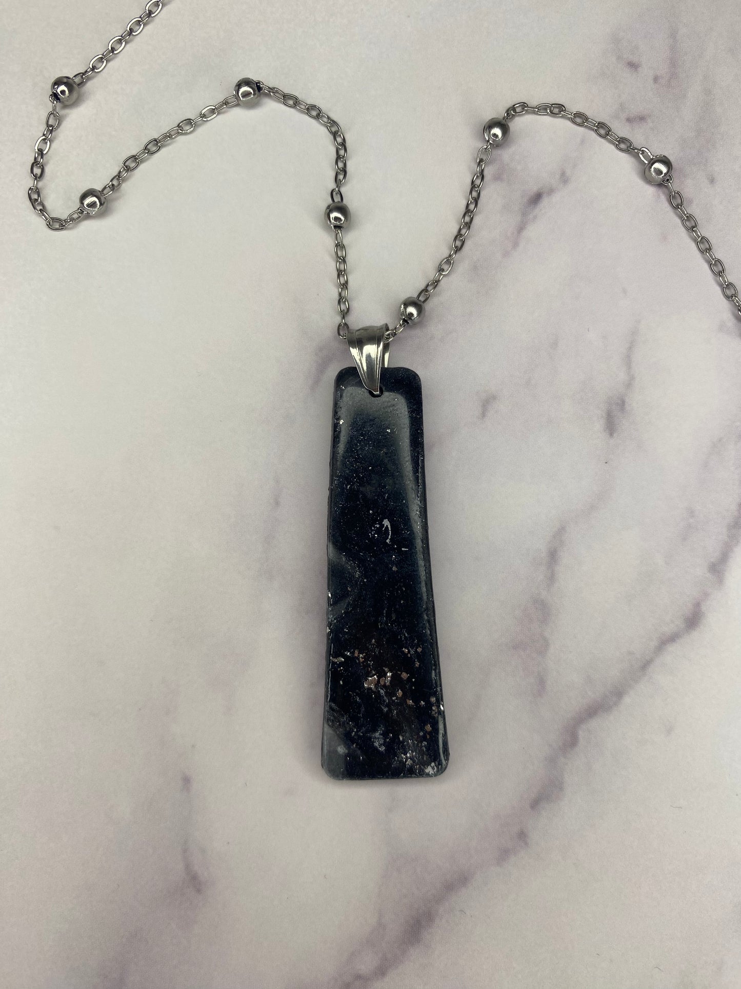 Collana pendente con ciondolo rettangolare, in porcellana fredda, colore nero con dettagli in argento, effetto marmo, con catenina argentata. 
Gioiello artigianale fatto a mano da persone cieche e ipovedenti. 