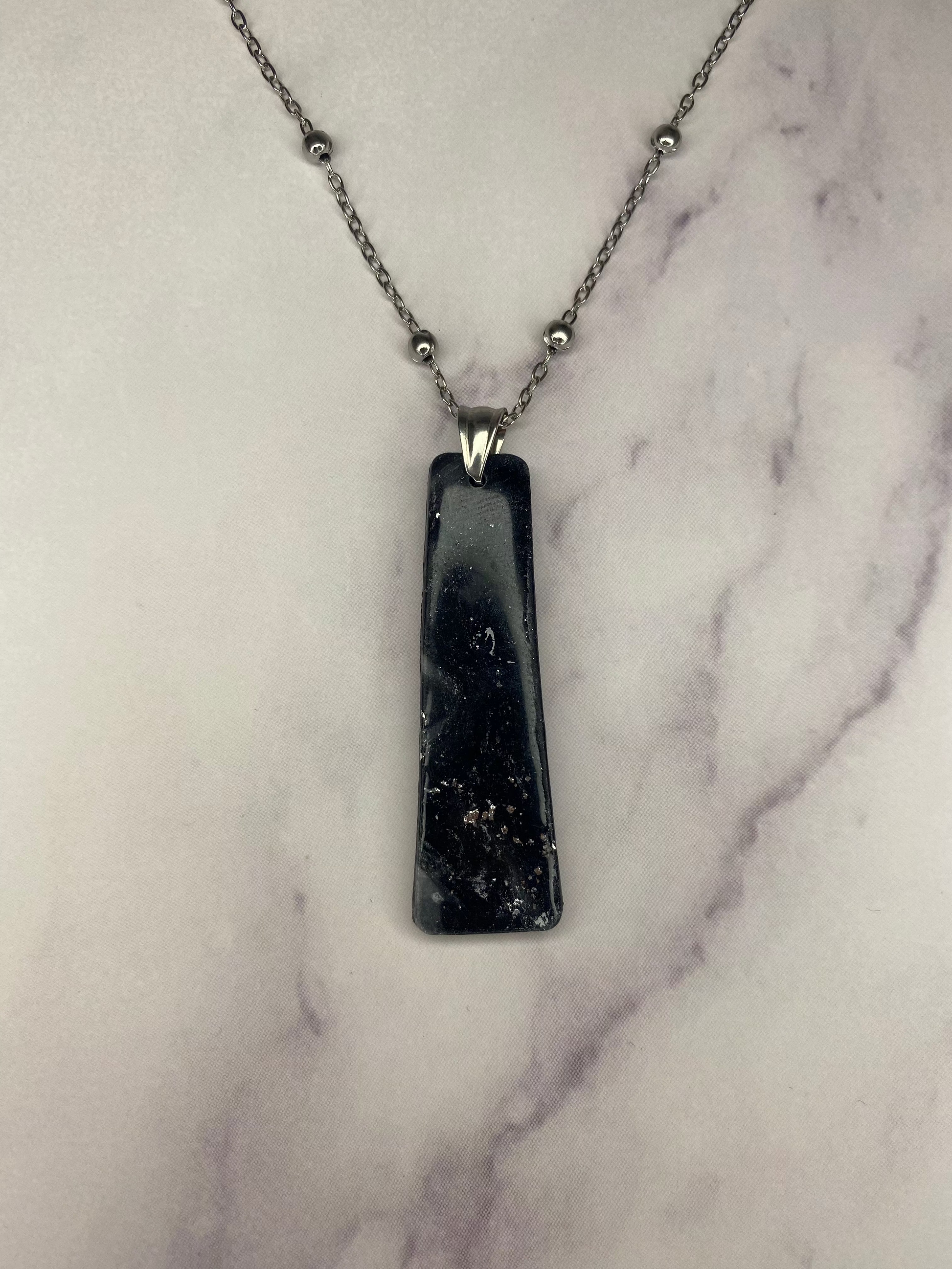 Collana pendente con ciondolo rettangolare, in porcellana fredda, colore nero con dettagli in argento, effetto marmo, con catenina argentata. 
Gioiello artigianale fatto a mano da persone cieche e ipovedenti. 