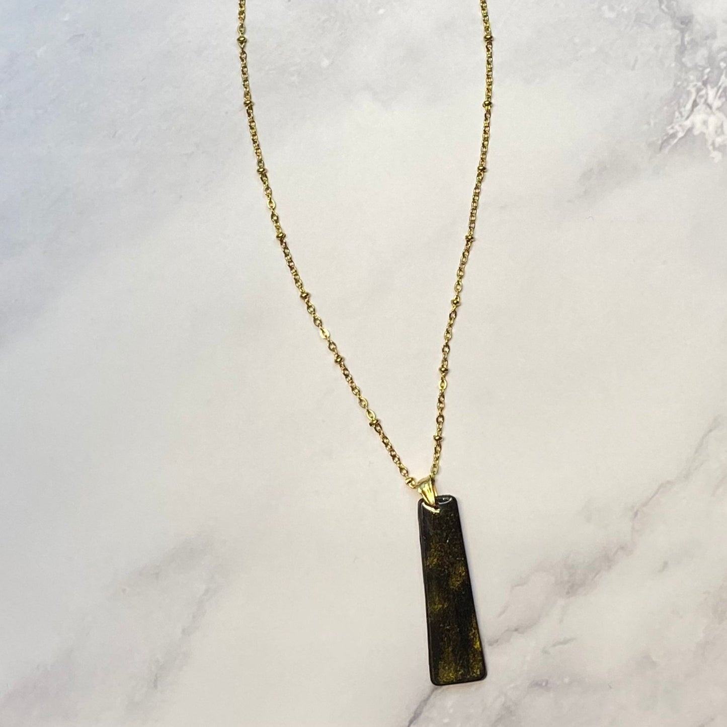 Collana pendente con ciondolo rettangolare allungato in porcellana fredda, colore nero e oro, con catenina dorata.