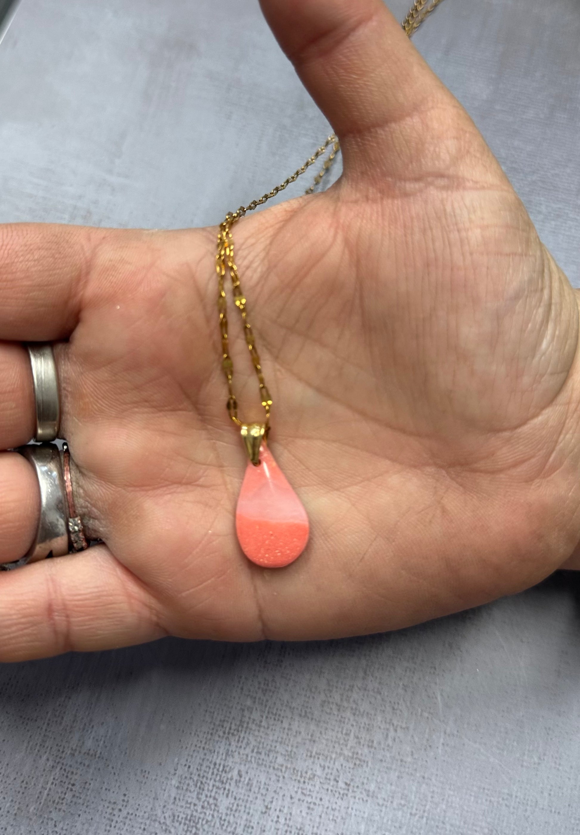 Collana a goccia, rosa corallo in porcellana fredda, sul palmo di una mano. Gioiello realizzato da artigiani ciechi e ipovedenti.