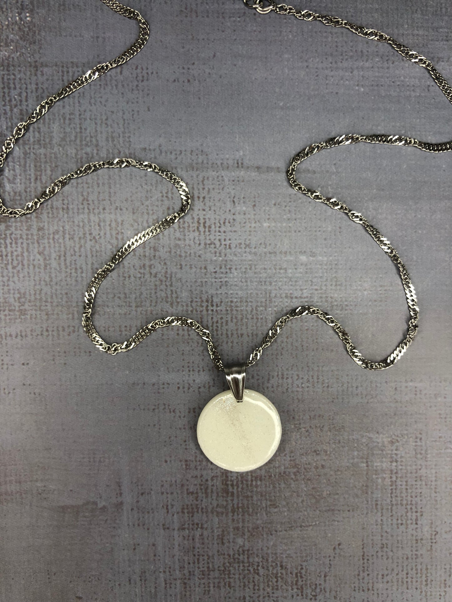 Collana pendente con ciondolo a forma di cerchio, in porcellana fredda, colore bianco con dettagli in argento, con catenina argentata. 
Gioiello artigianale fatto a mano da persone cieche e ipovedenti.