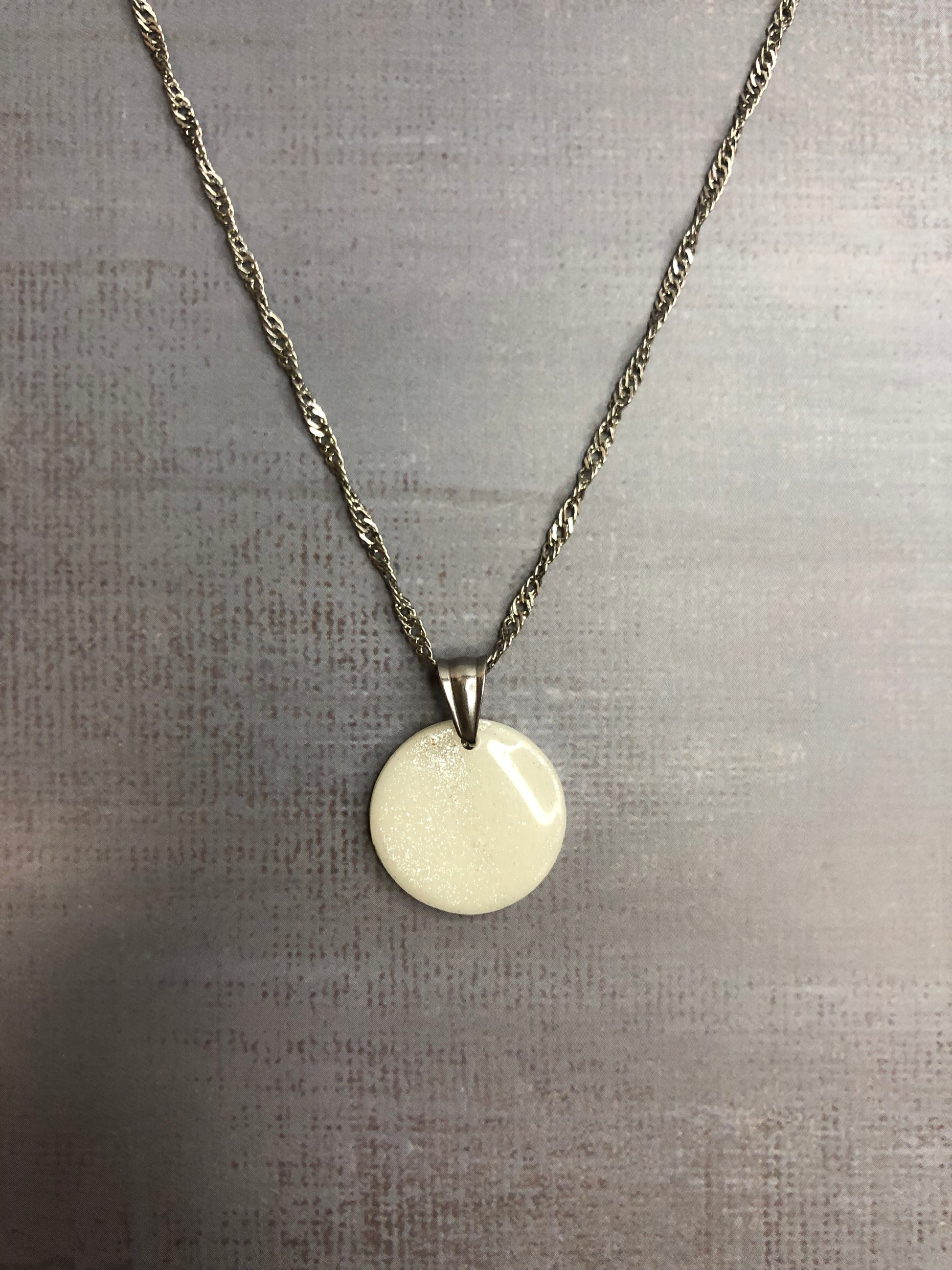 Collana pendente con ciondolo a forma di cerchio, in porcellana fredda, colore bianco con dettagli in argento, con catenina argentata. 
Gioiello artigianale fatto a mano da persone cieche e ipovedenti.