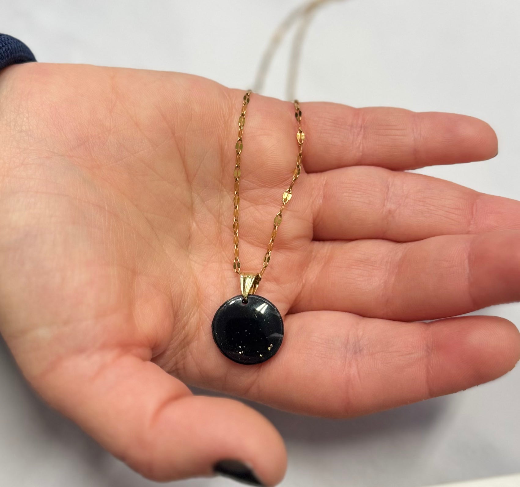 Collana con tondo nero intenso in porcellana fredda, tenuta sul palmo di una mano. Gioiello realizzato da artigiani ciechi e ipovedenti