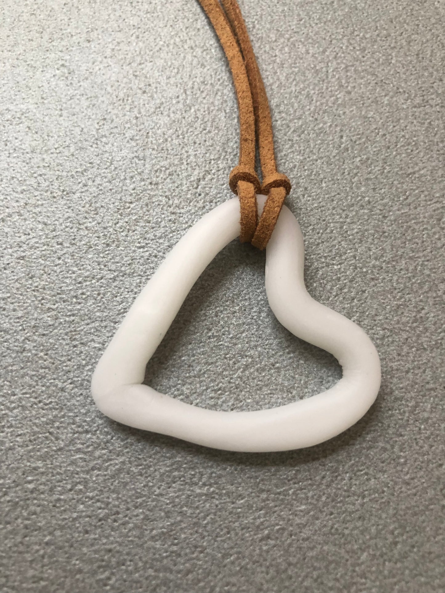 Primo piano del ciondolo a cuore in porcellana bianca con cordino marrone chiaro, collana “Cuore Imperfetto” collezione Asimmetrie