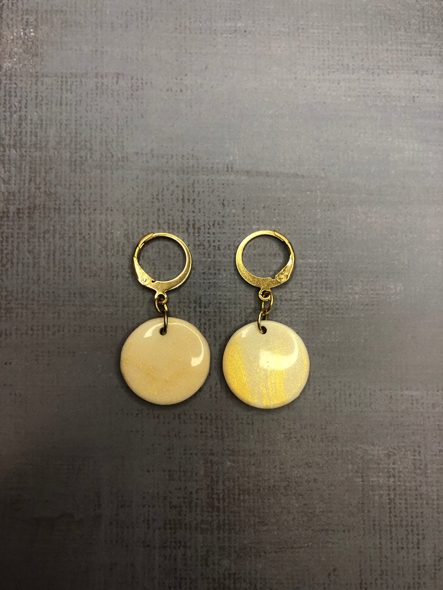 Orecchini pendenti artigianali in porcellana fredda a forma di cerchio, colore bianco con sfumature oro, con gancio a cerchio a leva dorato. 
Gioiello realizzato a mano da artigiani ciechi e ipovedenti.