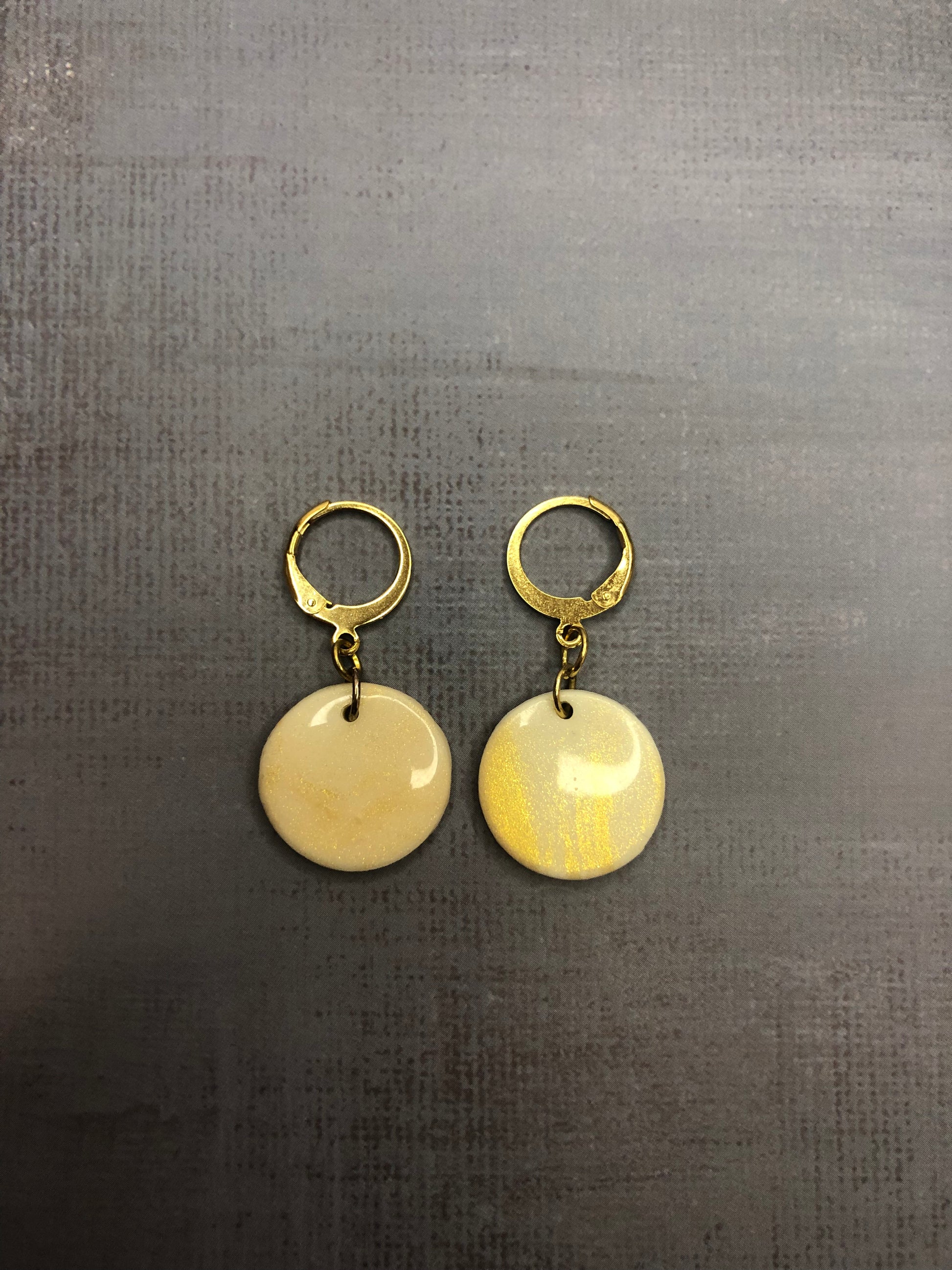Orecchini pendenti artigianali in porcellana fredda a forma di cerchio, colore bianco con sfumature oro, con gancio a cerchio a leva dorato. 
Gioiello realizzato a mano da artigiani ciechi e ipovedenti.