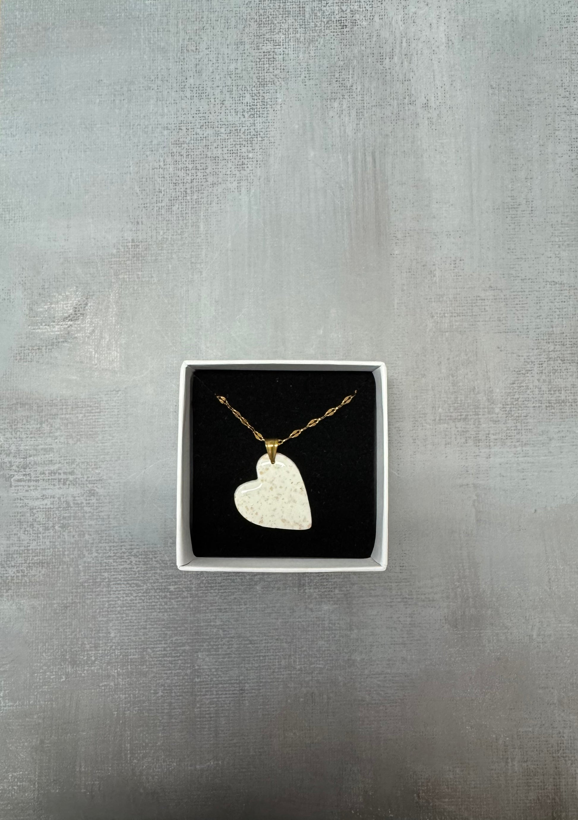 Confezione regalo aperta Myra Lab con collana pendente a cuore in porcellana fredda bianca a pois dorati. Gioiello artigianale fatto a mano da persone cieche e ipovedenti.
