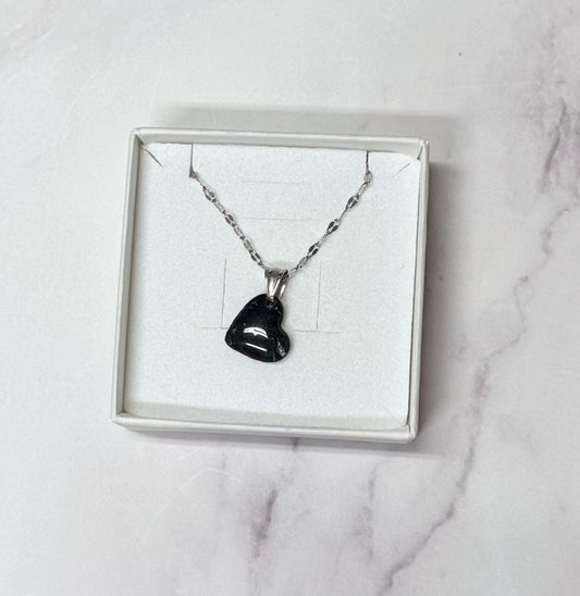 Confezione originale Myra Lab aperta, contenente collana con ciondolo a forma di cuore, di colore nero con leggere sfumature argentate, in porcellana fredda. Gioiello artigianale realizzato da persone cieche e ipovedenti.