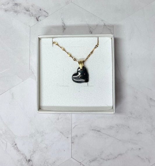 Confezione originale Myra Lab aperta, contenente la collana con ciondolo a forma di cuore, nero sfumato, in porcellana fredda. Gioiello artigianale realizzato da persone cieche e ipovedenti.