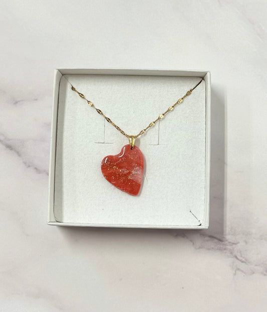 Confezione originale Myra Lab aperta, contenente la collana con cuore rosso marmorizzato in porcellana fredda con leggere sfumature dorate. Gioiello artigianale realizzato da persone cieche e ipovedenti.