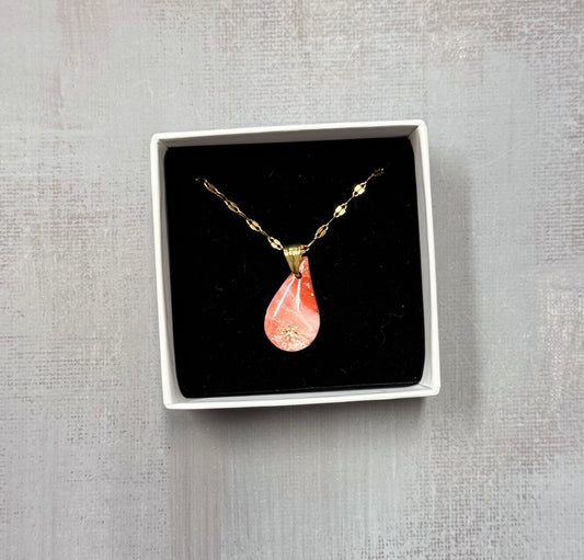 Confezione originale Myra Lab aperta, contenente la collana dorata con ciondolo a forma di goccia rosa marmorizzato, con leggere sfumature dorate, in porcellana fredda. Gioiello artigianale realizzato da persone con disabilità visiva.