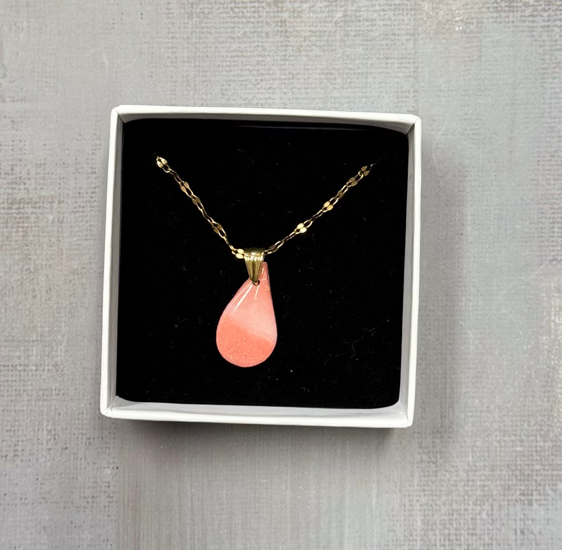 Confezione originale Myra Lab aperta, contenente collana con ciondolo a goccia, rosa corallo in porcellana fredda. Gioiello realizzato da artigiani ciechi e ipovedenti.