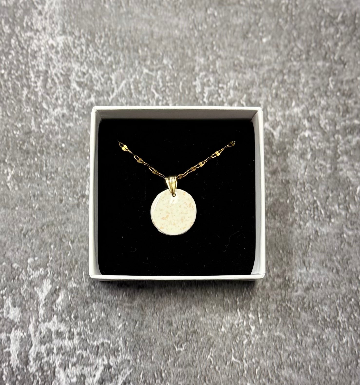 Confezione originale Myra Lab aperta, contenente la collana con pendente tondo bianco con pallini dorati, in porcellana fredda. Gioiello artigianale realizzato da persone cieche e ipovedenti.